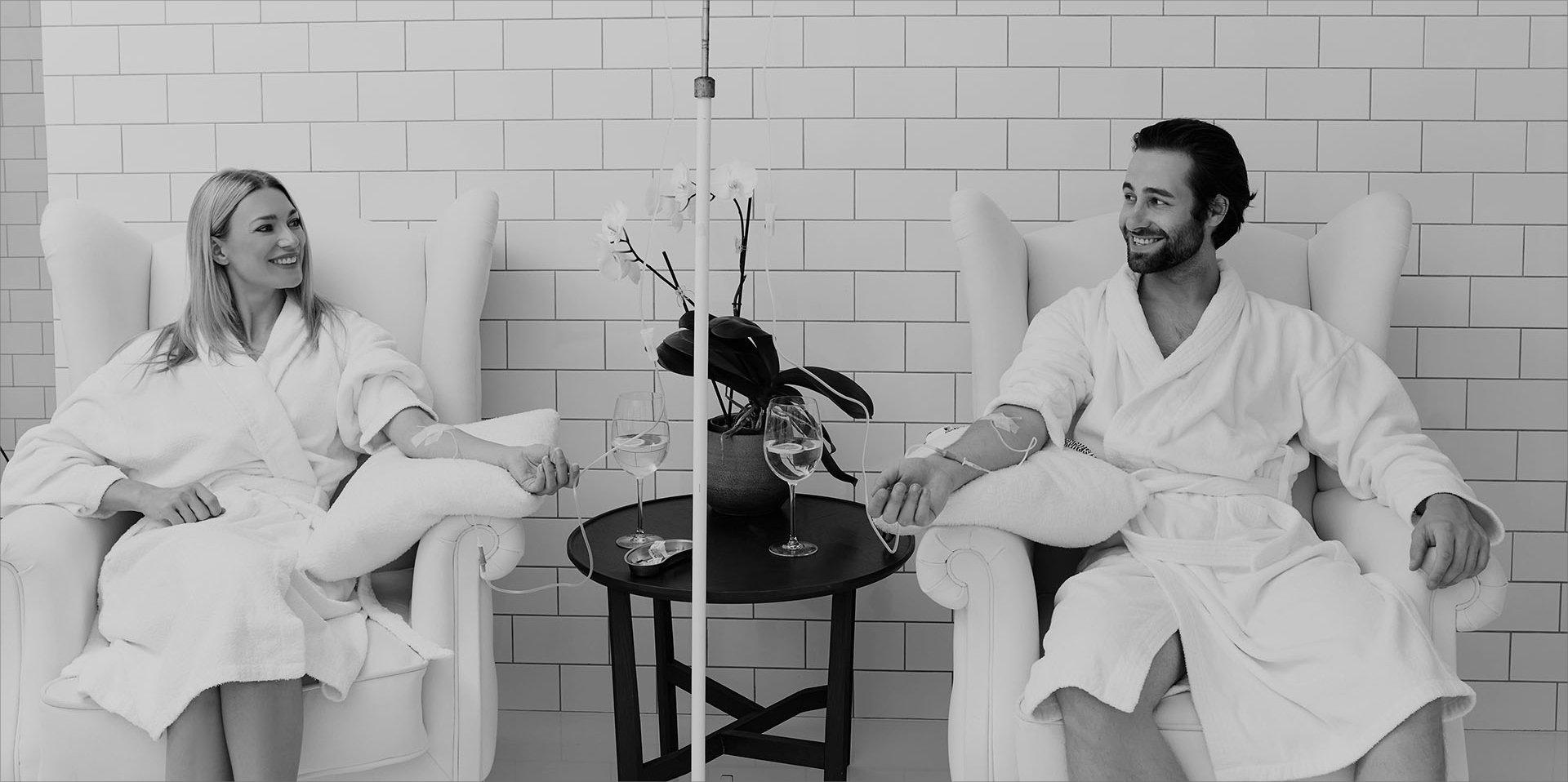 Two men sitting in white robes with wine glasses.
